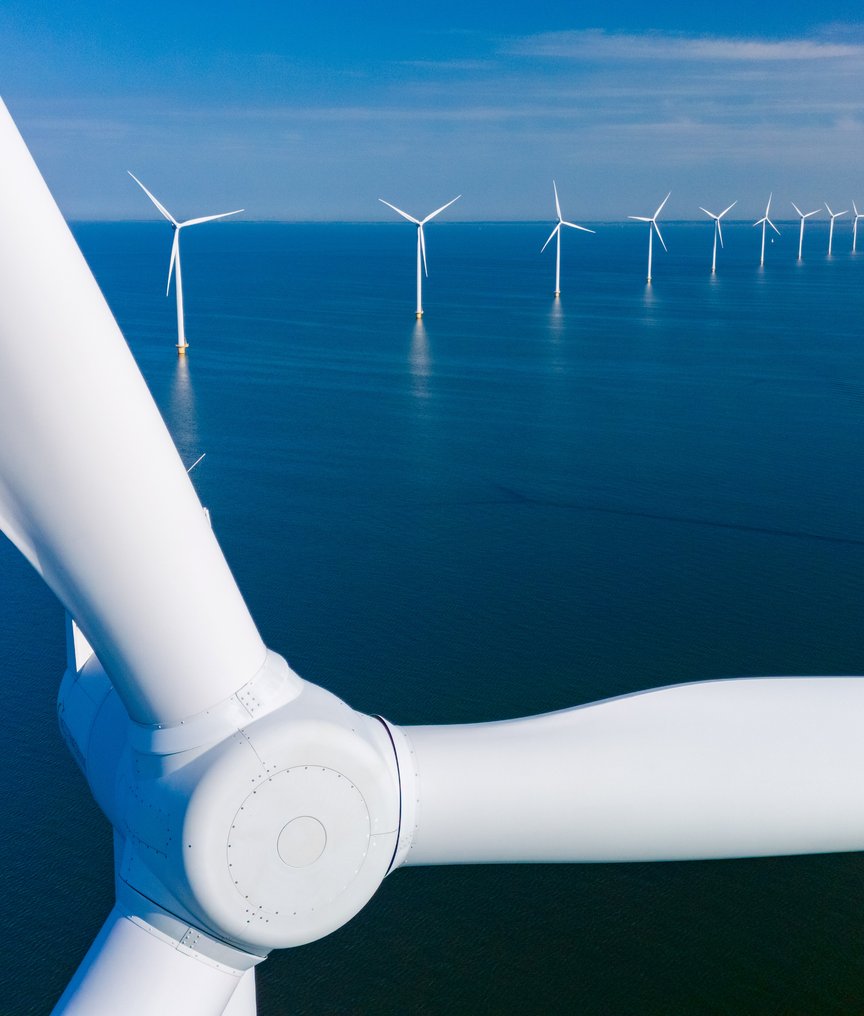 Aerial view of an offshore wind farm with multiple white wind turbines stretching across a calm blue