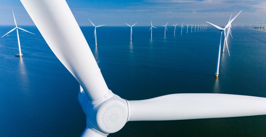 Aerial view of an offshore wind farm with multiple white wind turbines stretching across a calm blue